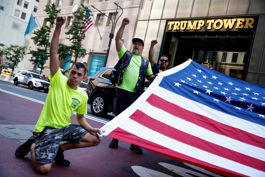 Men put their fist in the air and hold a large flag near a building with 'Trump Tower' written on it.