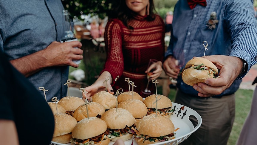 A plate of sliders with people reaching over to take one