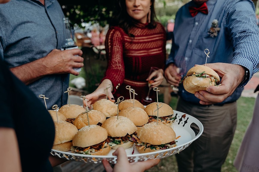 A plate of sliders with people reaching over to take one
