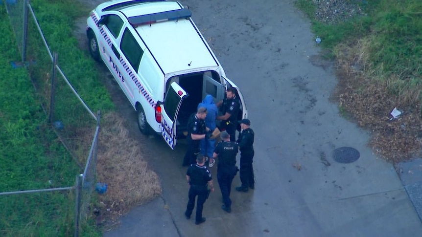 Aerial photo of police officers with a man in custody next to a police vehicle.