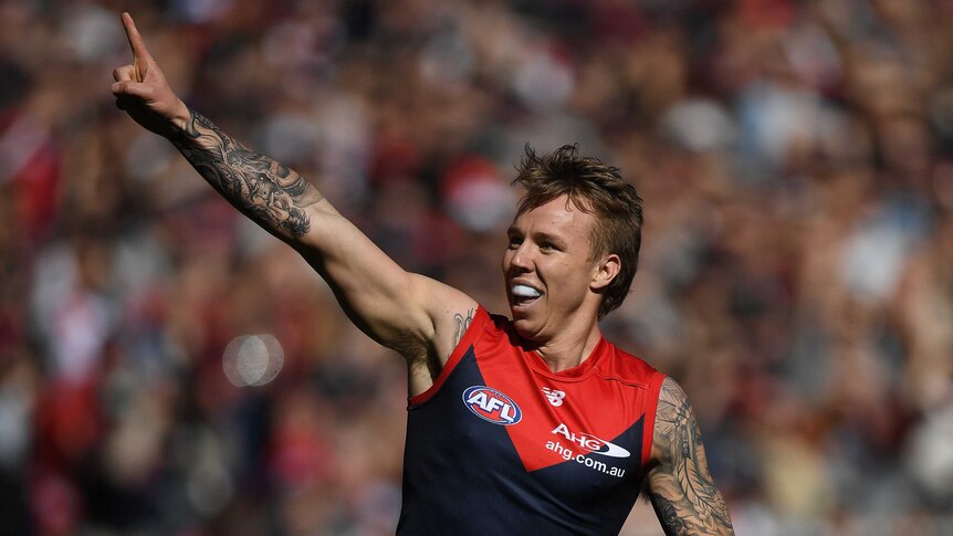 James Harmes smiles and points to the crowd with his right arm after kicking a goal for the Demons.