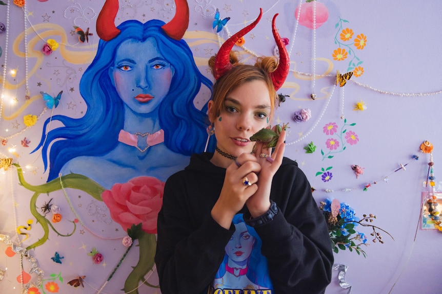 A young woman poses with a frog on her hand, while wearing horns. 