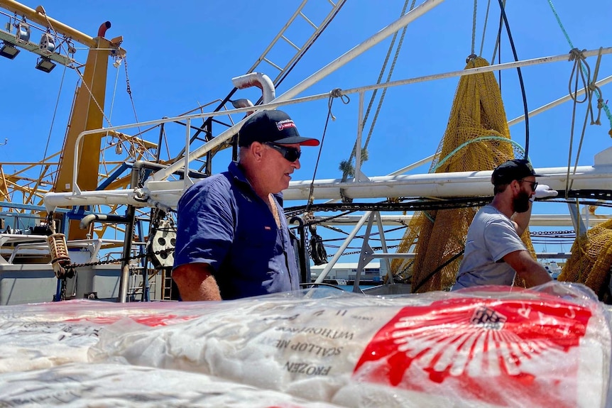 An older man in a hat and sunglasses works on a fishing boat.