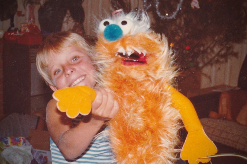 Child in front of a Christmas tree holding a large yellow furry muppet toy