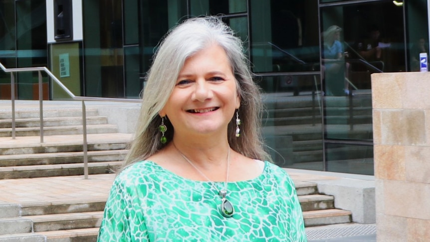 Penny Burke standing outside of the University of Newcastle, smiling, wearing green shirt