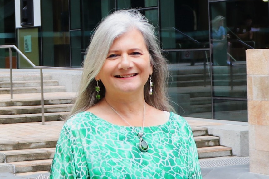 Penny Burke standing outside of the University of Newcastle, smiling, wearing green shirt