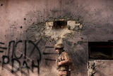 A soldier walks by a building which was hit by a large caliber mortar shell