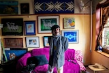 Mr Gawronski, a public housing tenant, standing in his apartment. A collection of his art is behind him on the wall.