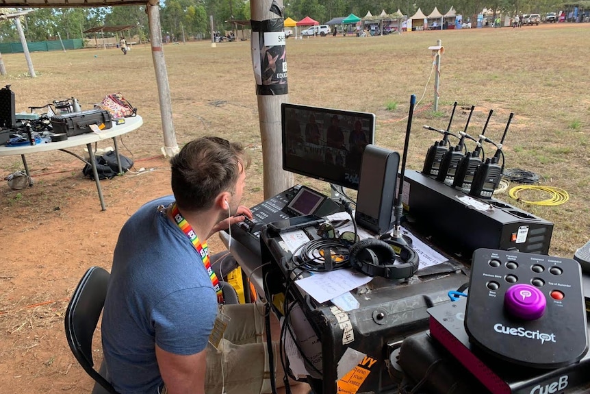 George sitting at desk operating TV equipment in bush setting.