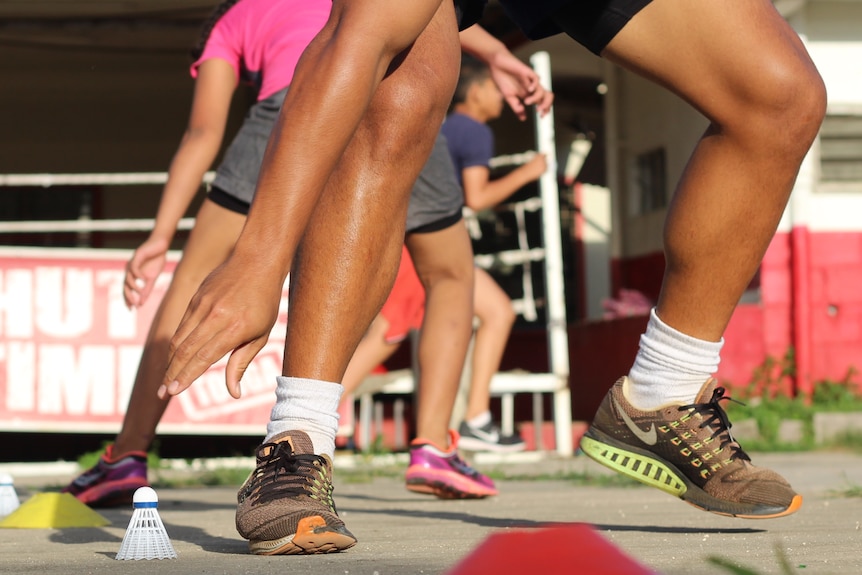 A close up of a man's legs during as he bends to pick up a shuttlecock