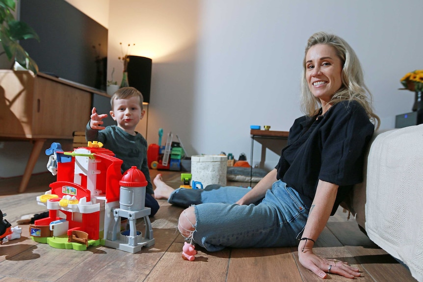Dee Behan sits next to son Max on the loungeroom floor. Max has a colourful plastic castle in front of him.