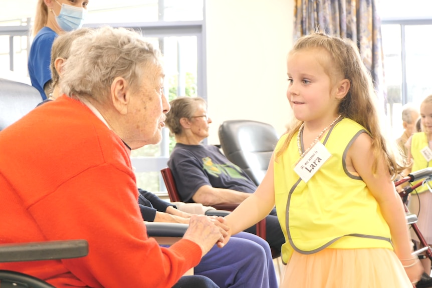 A young girl holds an older woman's hand in a retirement home.