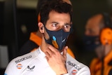 Race driver out of his car looks on while wearing a face mask. 