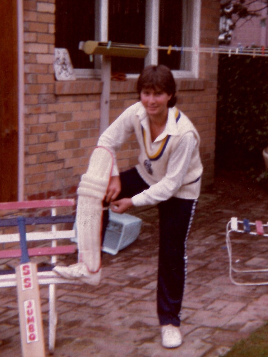 A young man poses for the camera while putting a cricket pad on his leg