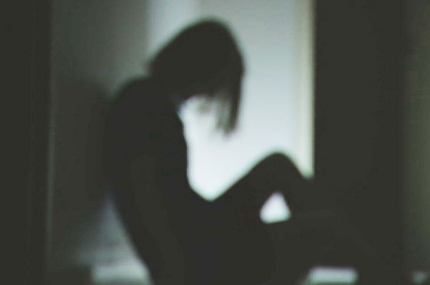 Woman in silhouette sitting down in hallway with head down.