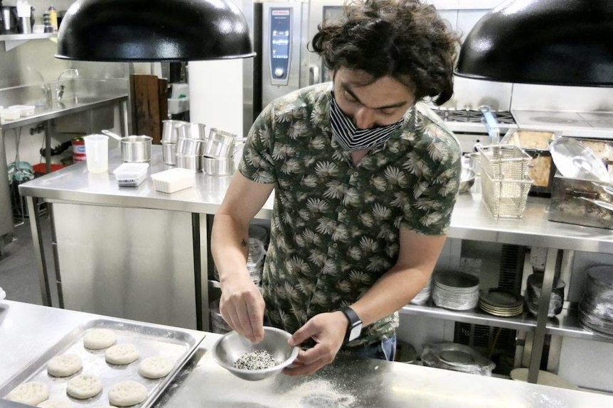 A man in a facemask prepares food in a restaurant kitchen.