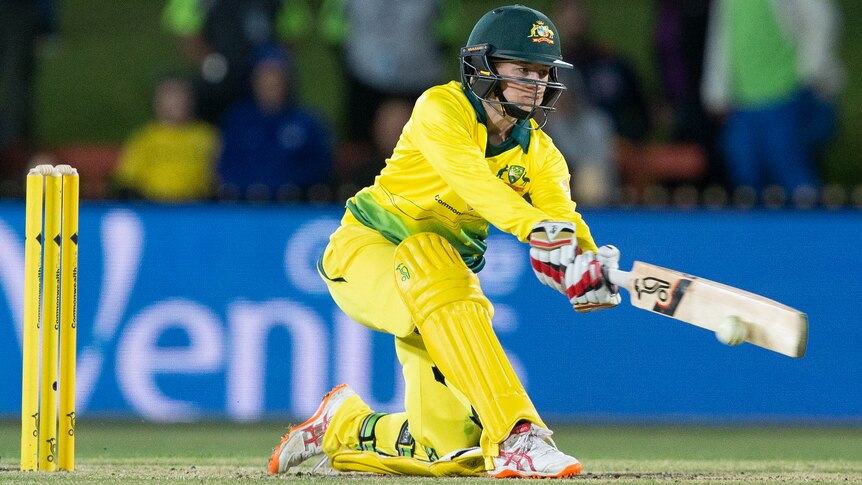 A female cricket player hits a sweep shot on one knee