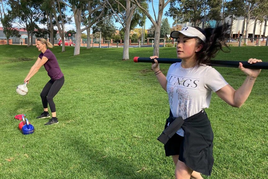Three women take part in an exercise class in a park.