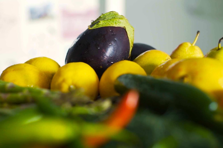 Photograph of vegetables piled on a table with eggplant at the centre.