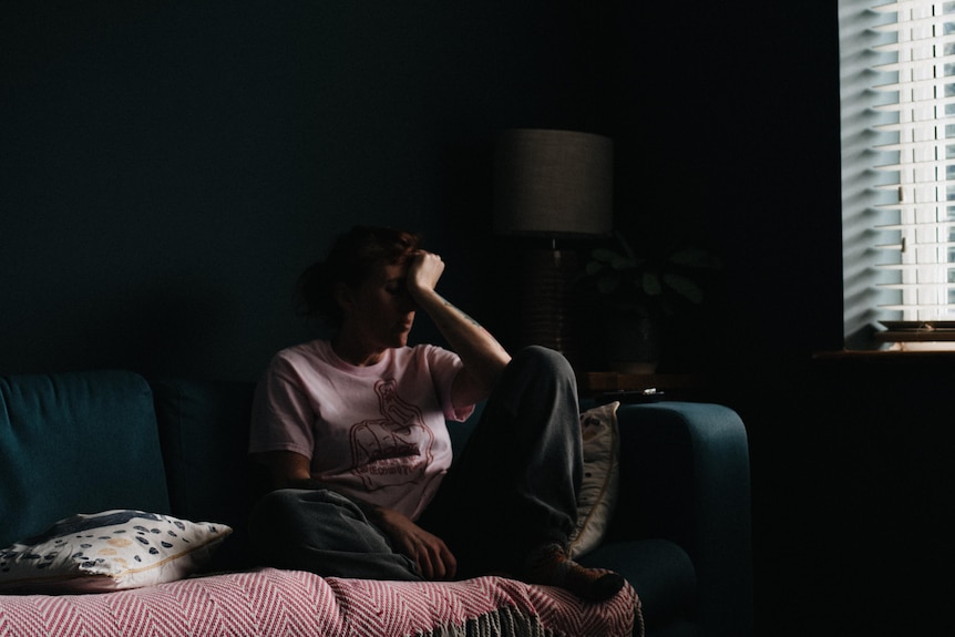 A woman rests her head on her hand in a darkened room