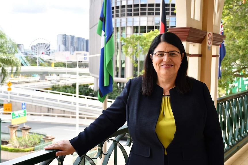 Grace Grace stands on a balcony in a building with the river behind her in the Brisbane CBD.