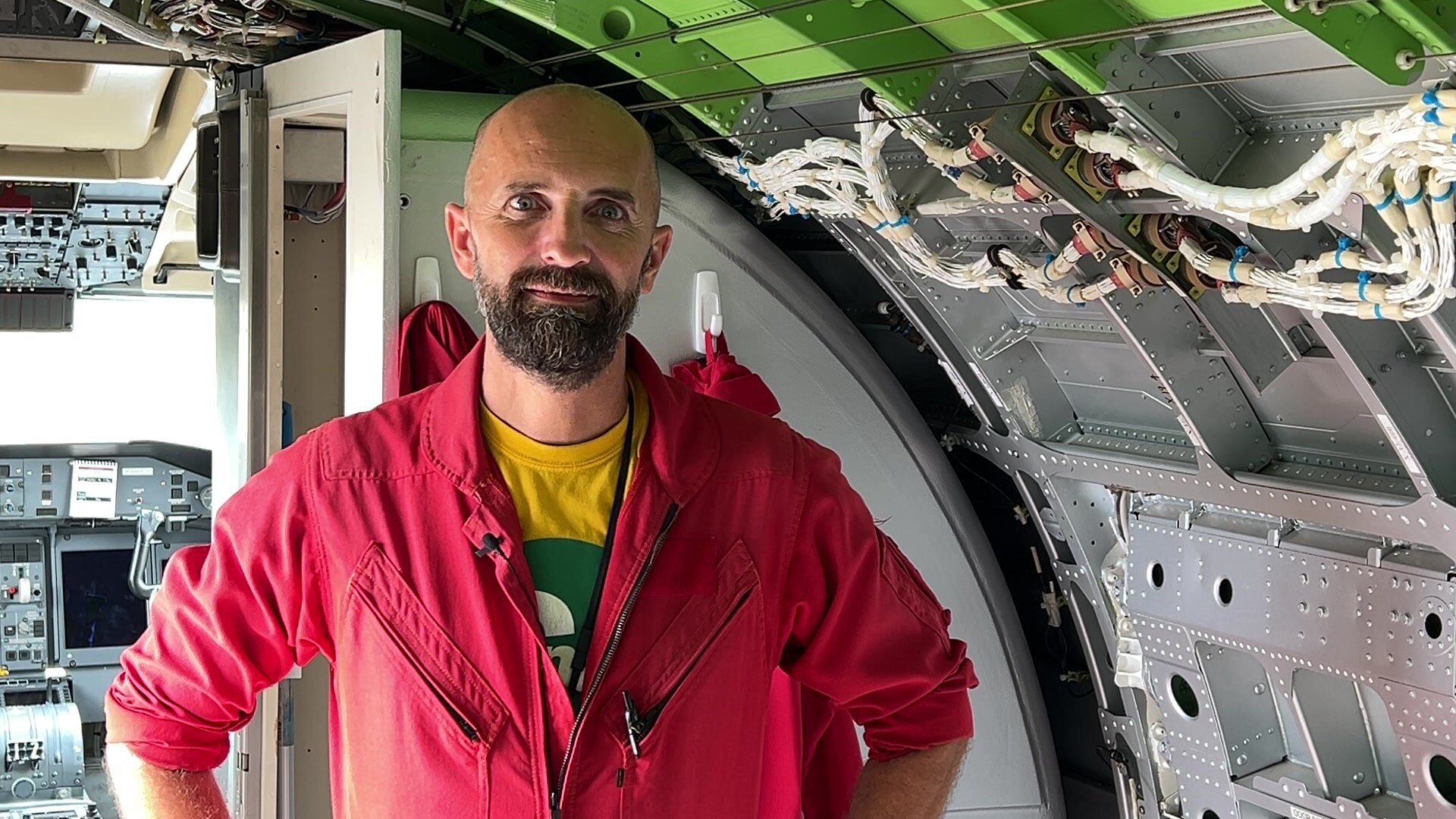 A man in a red flight suit standing outside the cockpit of a large plane.