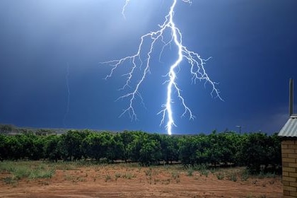 Large lightening strikes light up the night sky over a field.