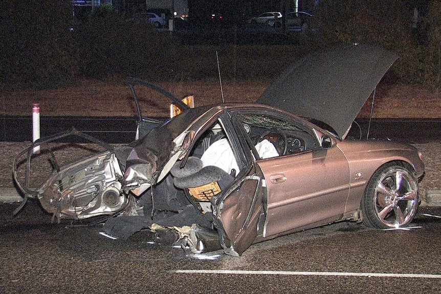 The front half of a car lies strewn on a road with its bonnet up after the vehicle split in two in a crash