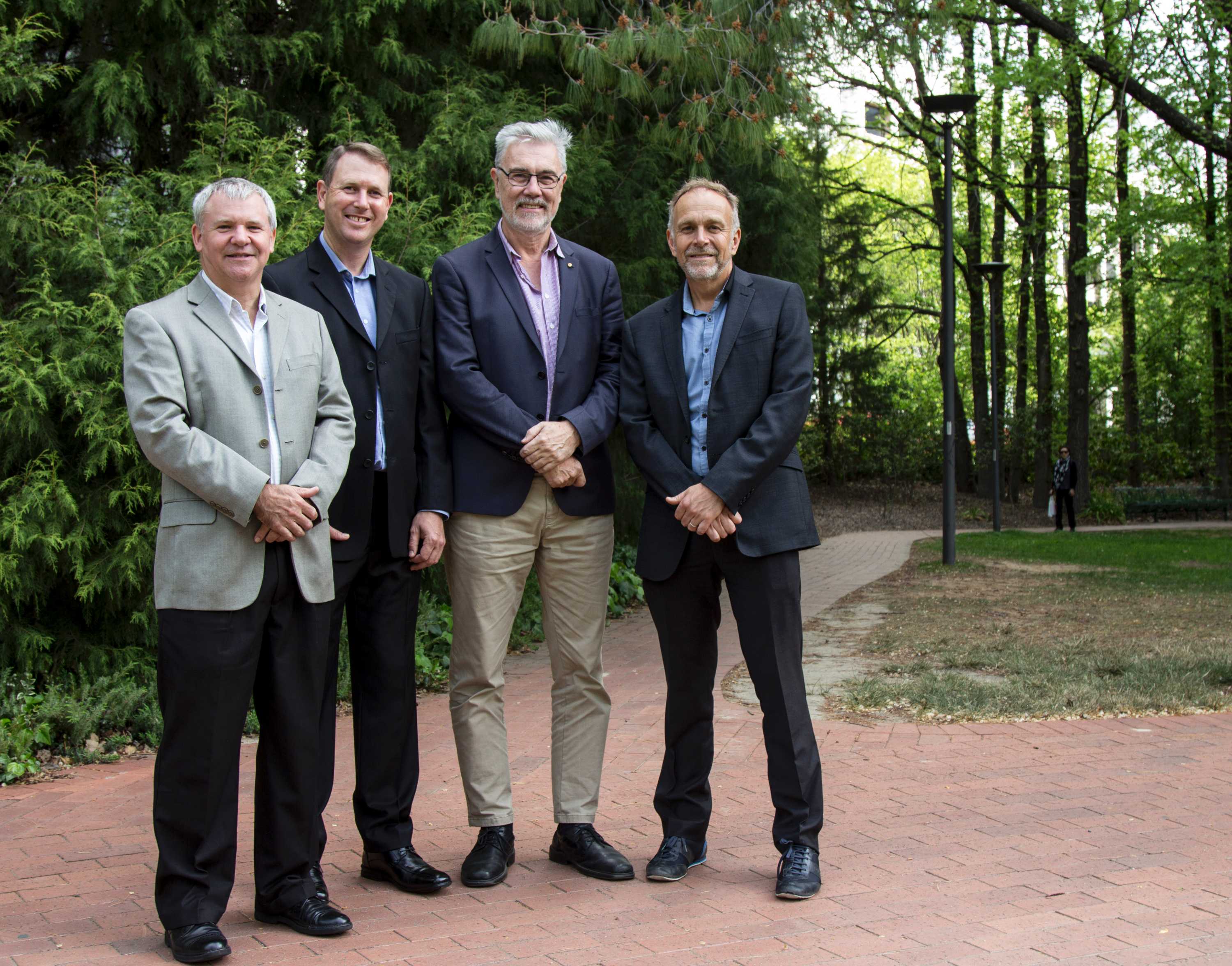 Four men stand together in a park.