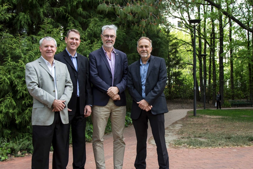 Four men stand together in a park.