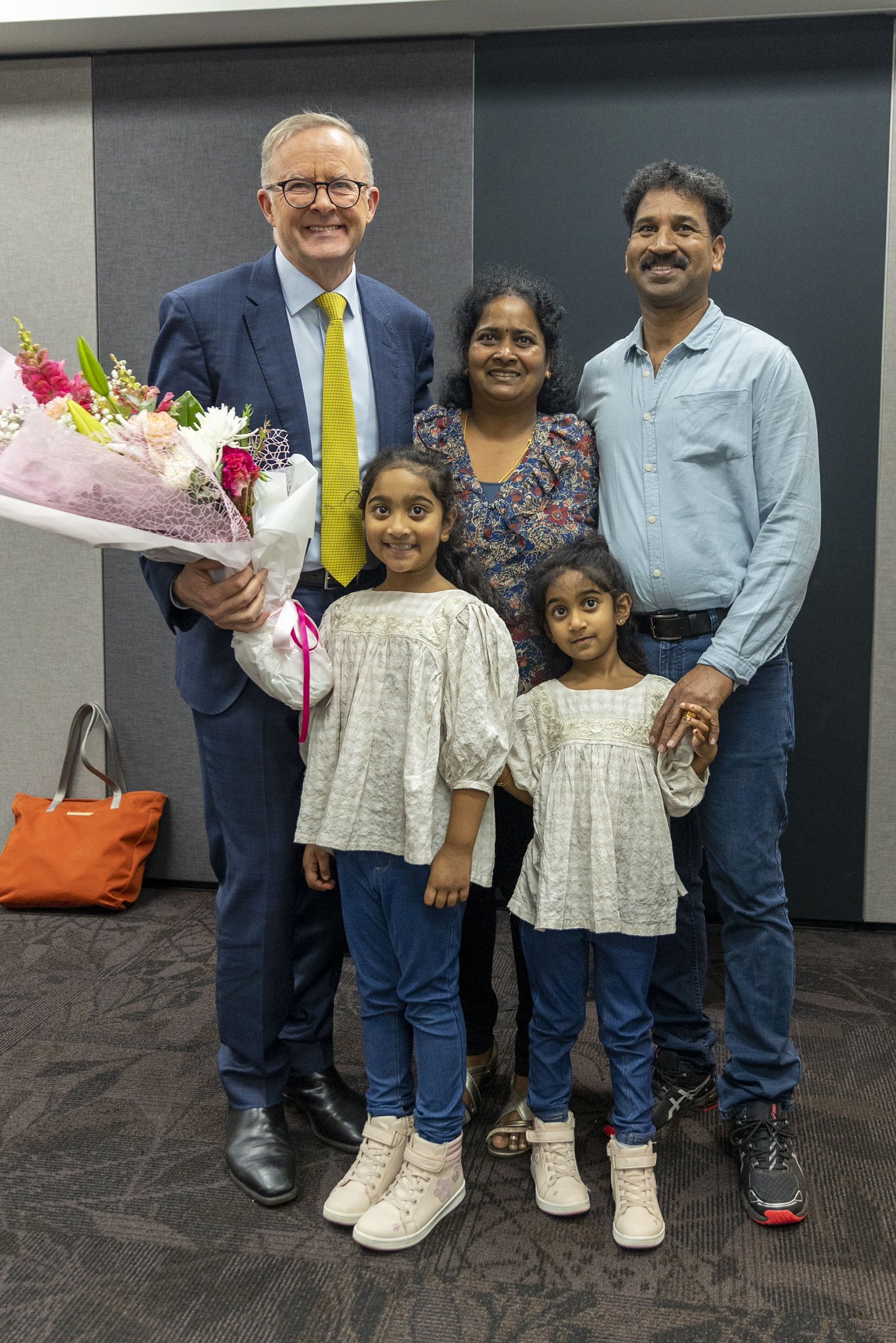 Two smiling men stand on either side of a smiling woman and two smiling little girls.