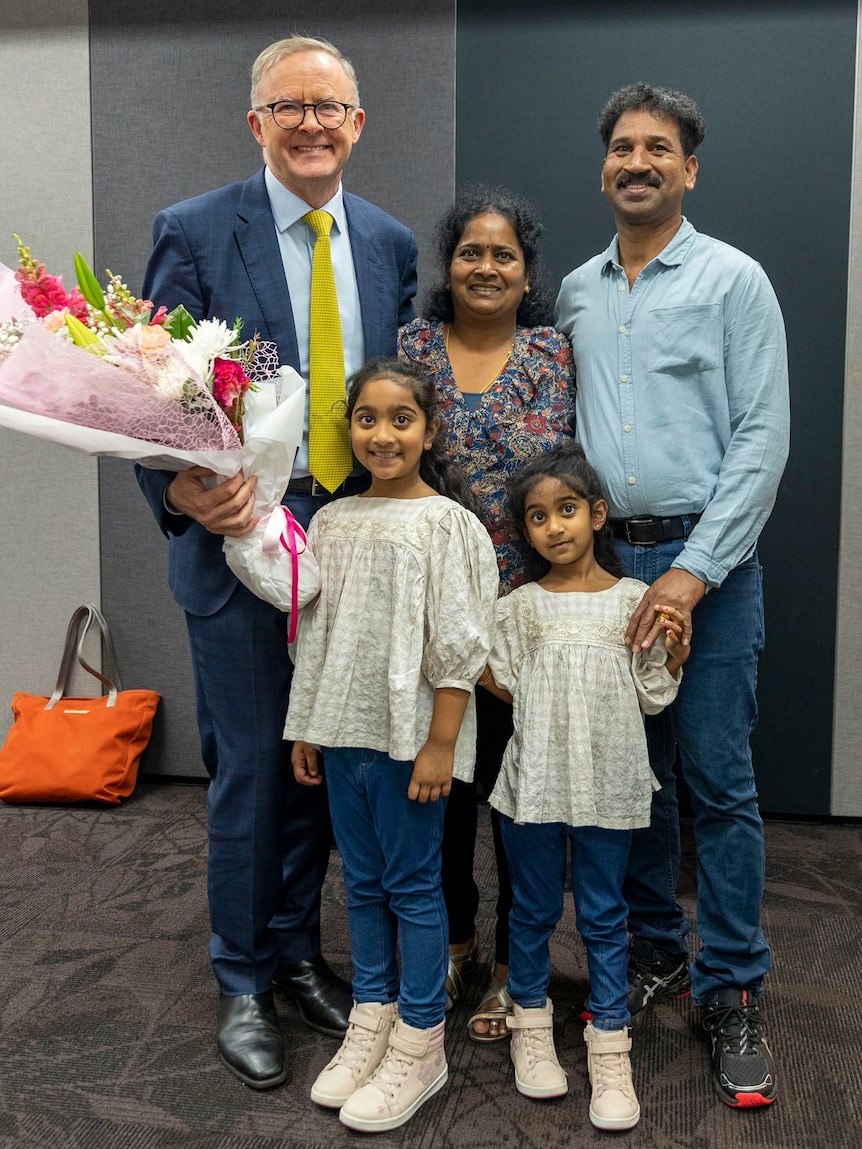 Two smiling men stand on either side of a smiling woman and two smiling little girls.