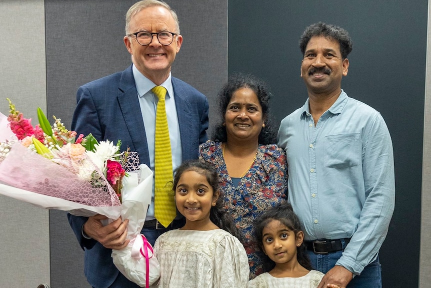 Two smiling men stand on either side of a smiling woman and two smiling little girls.