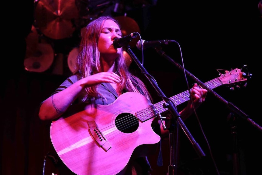 a woman at a dark stage playing a guitar