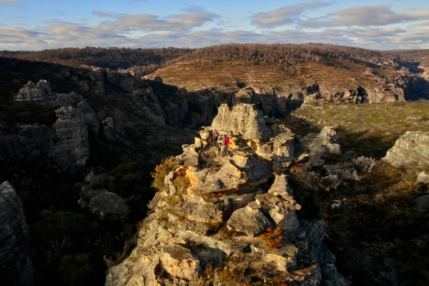 Two bush walkers perched on a rock formation in a vast landscape.