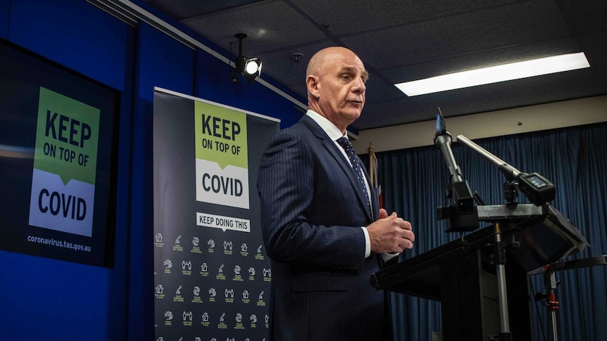 Tasmanian Premier Peter Gutwein stands behind a lectern with microphones attached at a press conference.