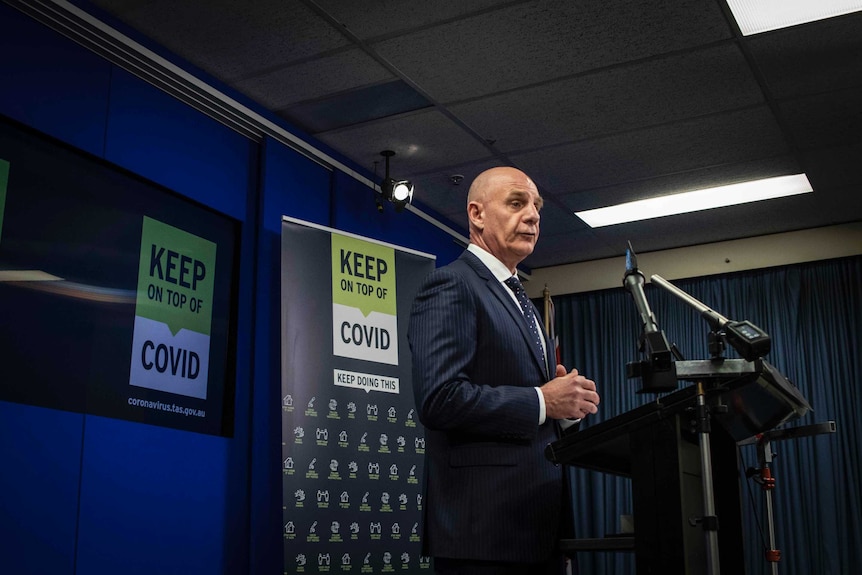 Tasmanian Premier Peter Gutwein stands behind a lectern with microphones attached at a press conference.