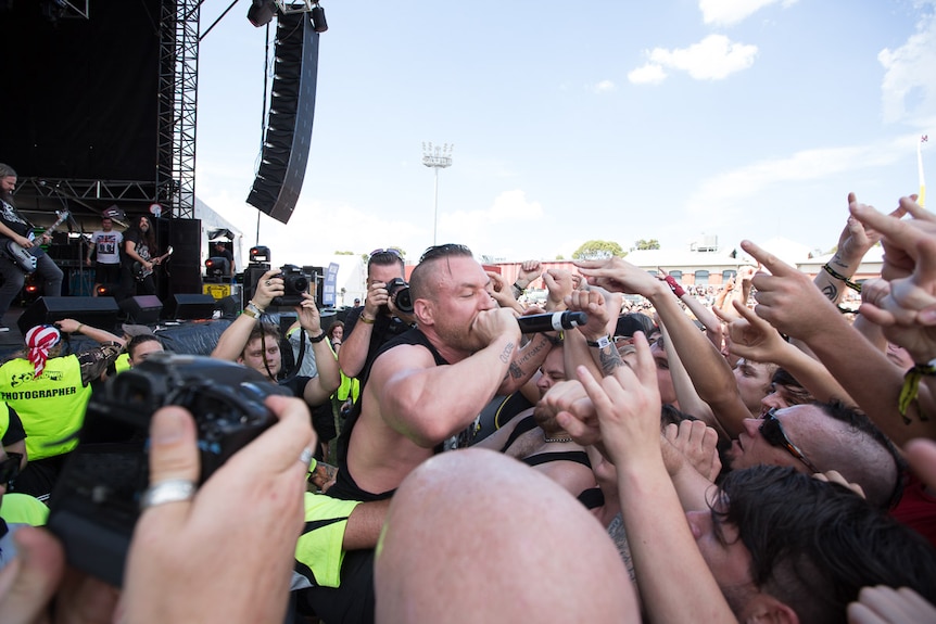 A male singer, surrounded by photographers, pushes into the front row of a large crowd