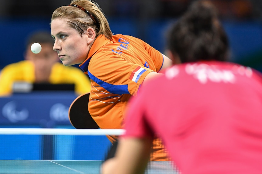 A Paralympic table tennis player eyes the ball in the air preparing to serve, as her opponent waits on other side of the net