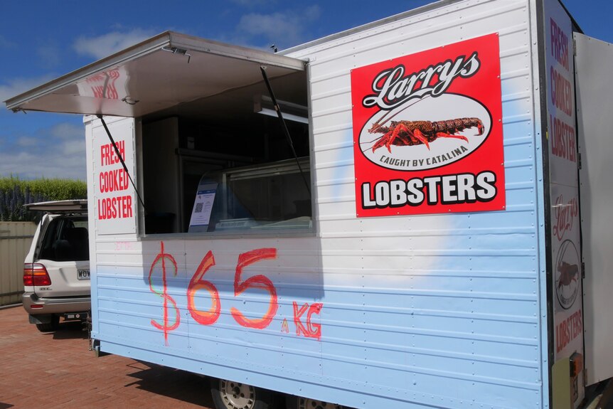A white and blue food truck red printed writing 'Fresh cooked lobster' & $65/kg in red marker & a big red Larrys Lobsters sign