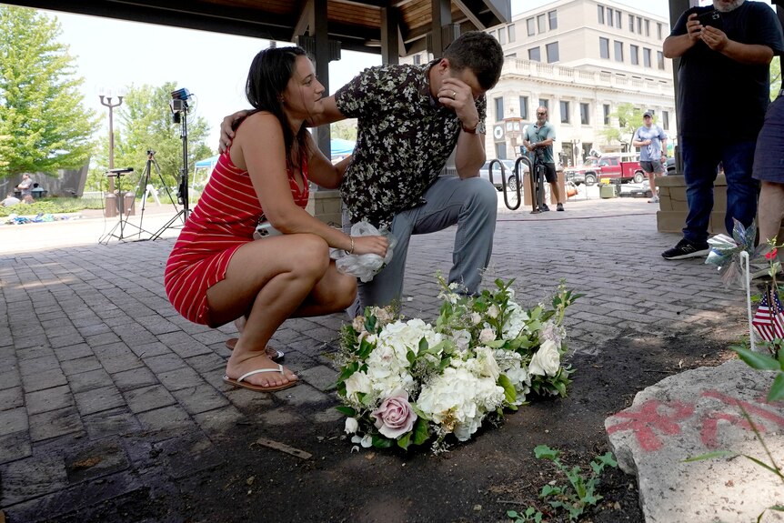 Молодой мужчина и женщина сидят возле цветов.  Мужчина закрывает лицо от боли