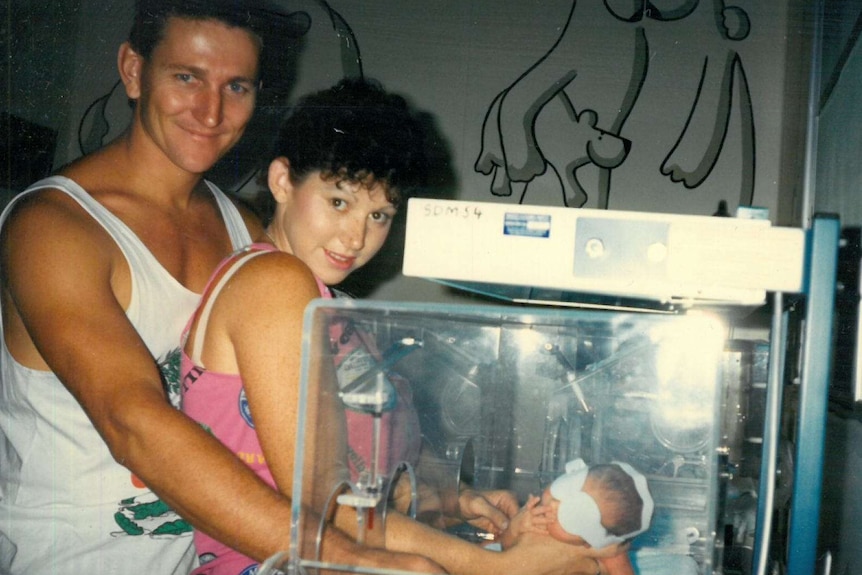 A man and woman stand next to a baby in an incubator