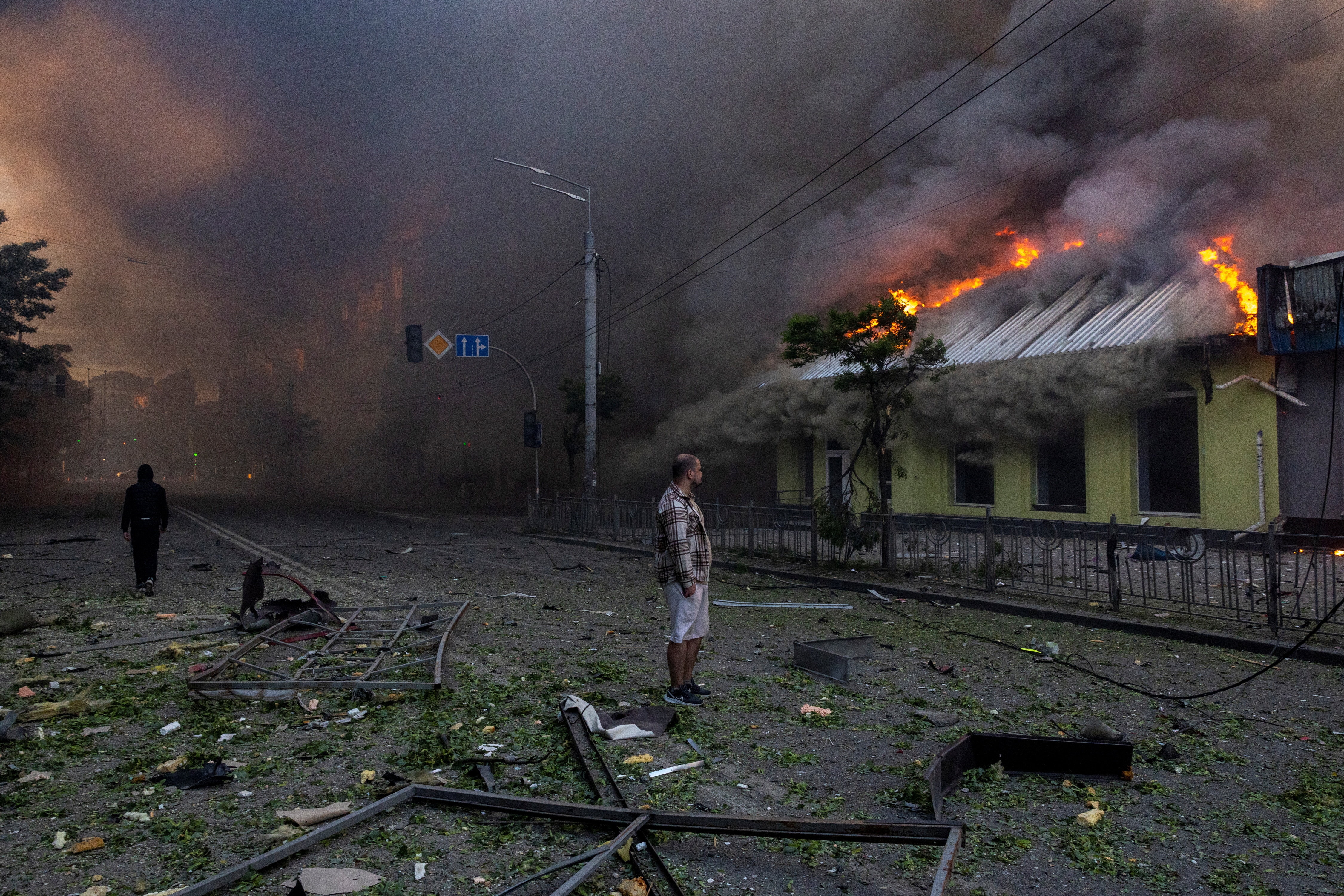 A man looks at his house with roof burning and smoke billowing all around him.
