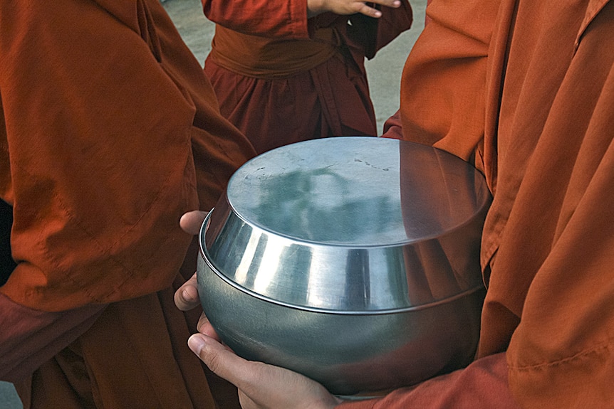 Locals bow their heads as they offer containers of freshly cooked food to the monks.