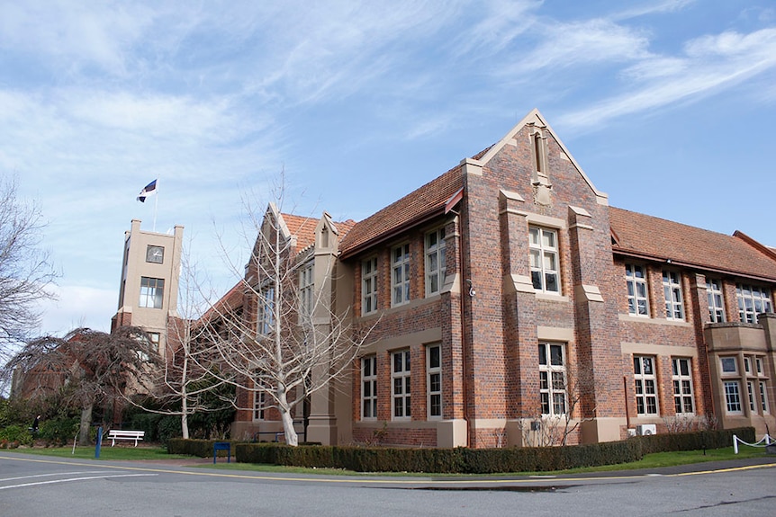 A two-storey, red-brick building with a taller bell tower along one frontage with a flag atop the glass-sided tower 