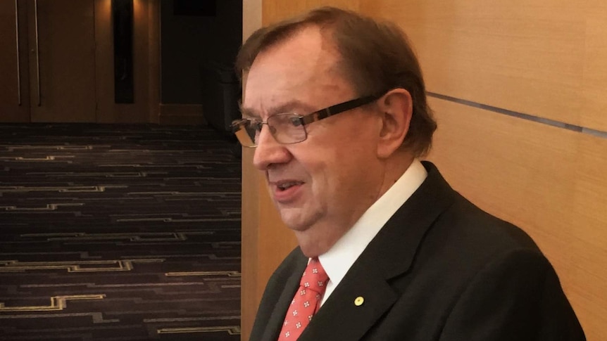 Harold Mitchell wearing a suit and tie and standing in the foyer of a hotel as he addresses the media