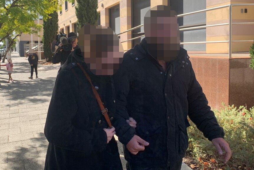 A couple walk arm in arm outside a court, followed by media, faces pixellated