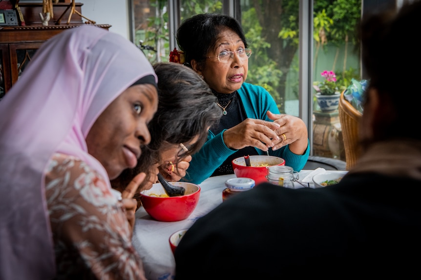 Thit and three women sitting eating laksa soup, Thit and a woman wearing a lilac-coloured hijab look at another while she talks.