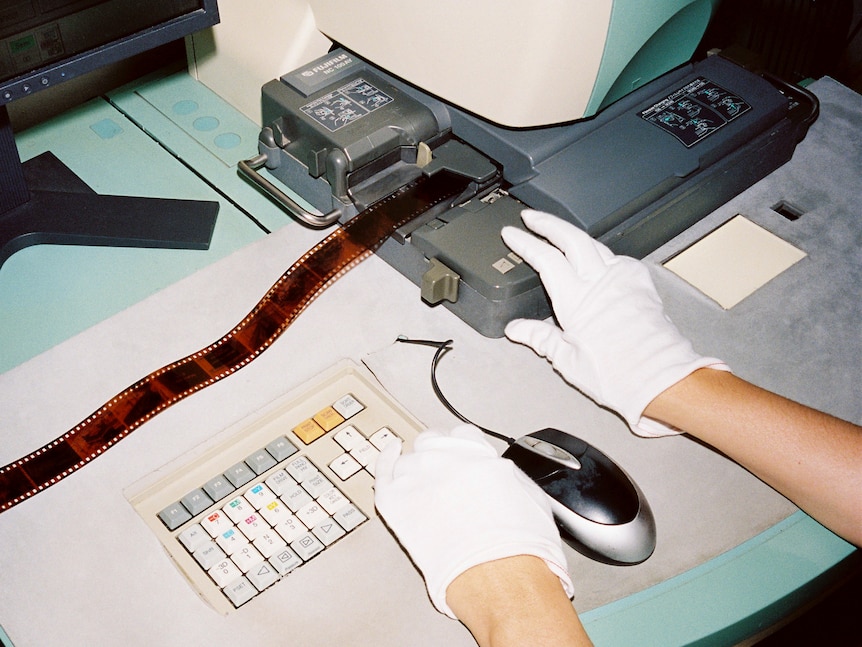  A film photo of a gloved hand printing brown negatives on film