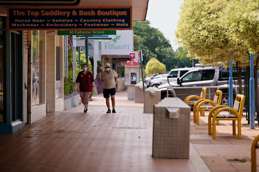 Two people wearing masks walking down an otherwise deserted street in the Katherine town centre.